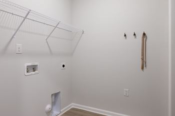 A white wall with a shelf and a few tools hanging on it.